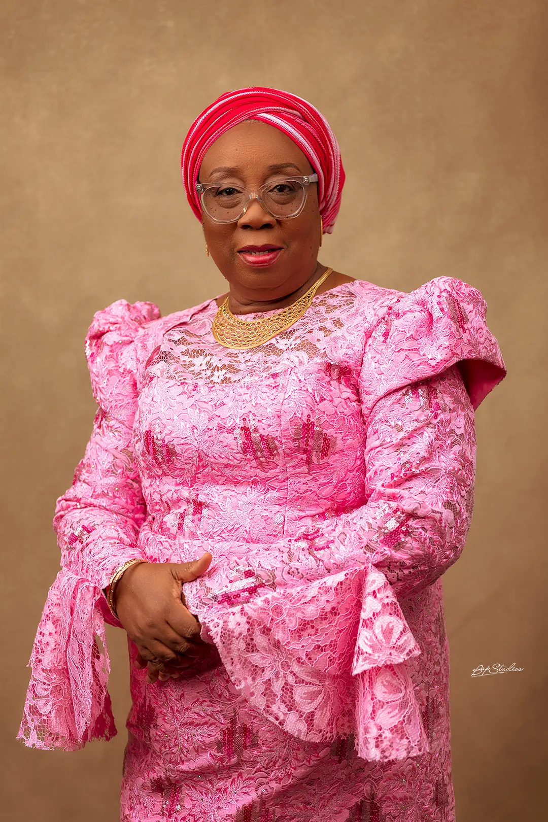 Folasade Adefisayo standing in a rose-pink lace ensemble with a matching head-tie.