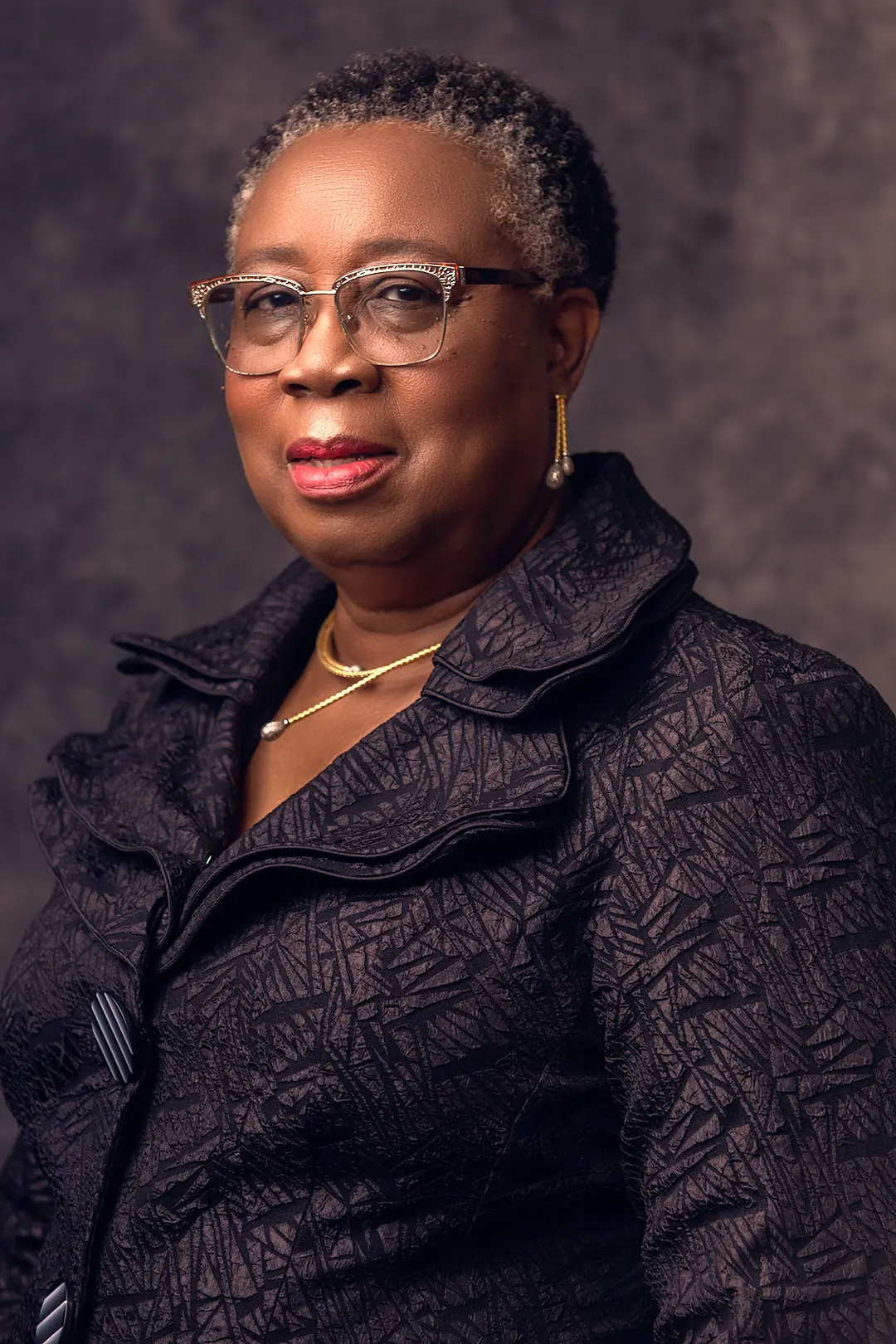 A low-key portrait of Folasade Adefisayo in a dark jacket against a near-black ground.